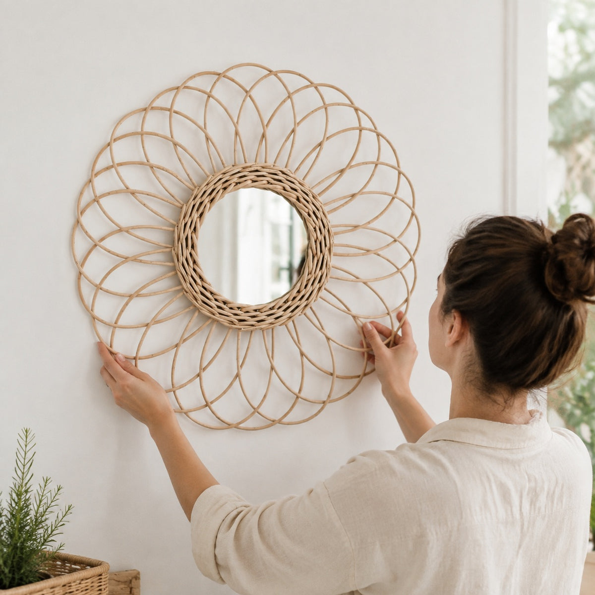 Mise en situation de l’installation d’un miroir décoratif en rotin naturel. Sa structure légère en forme de fleur apporte une finition artisanale et chaleureuse à la décoration murale.