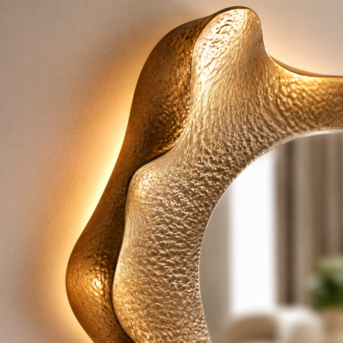 Gros plan sur le haut d’un miroir mural organique doré avec cadre sculpté texturé et éclairage LED, installé dans une entrée élégante.